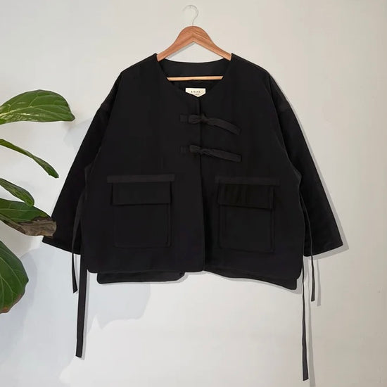 Black jacket with button details on a hanger against a white background