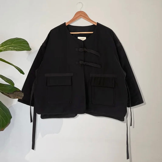 Black jacket with button details on a hanger against a white background