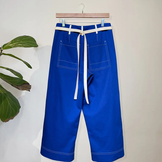Blue trousers with a white belt on a hanger against a light background