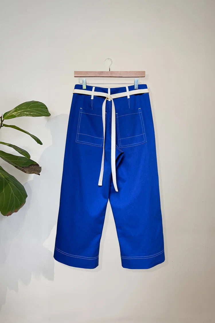 Blue trousers with a white belt on a hanger against a light background