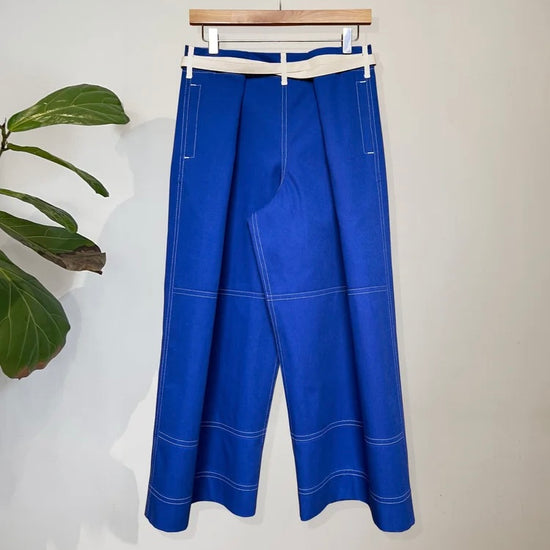 Blue trousers with white stitching on a hanger against a white background