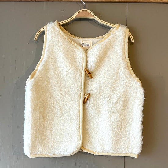 Cream fleece wool boxy fit waistcoat with brown toggle fastenings and darker cream piping on a grey background