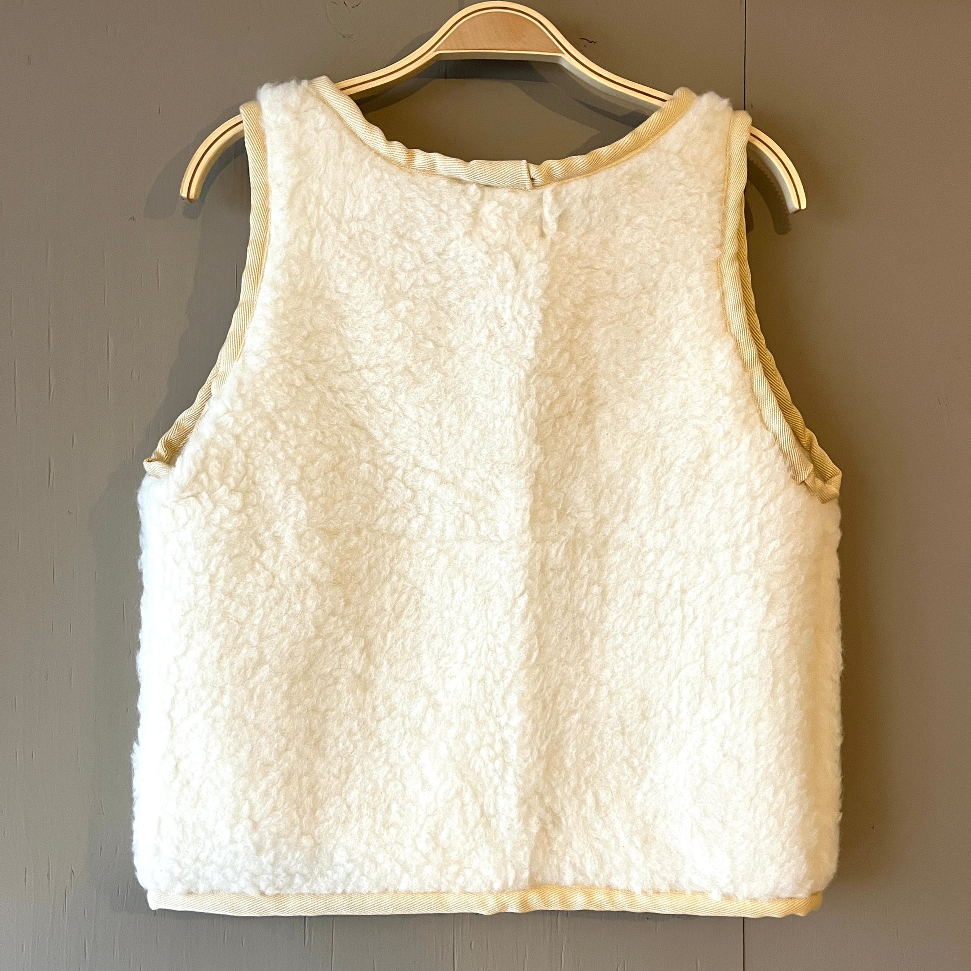 Back of a cream fleece boxy fit wool waistcoat with darker cream piping on a grey background