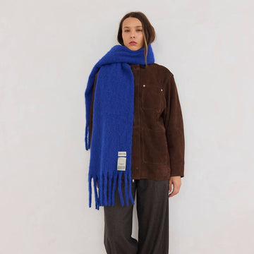 A woman wearing a brown outfit on a white background with a blue scarf