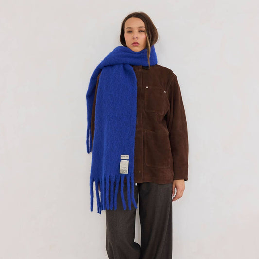 A woman wearing a brown outfit on a white background with a blue scarf