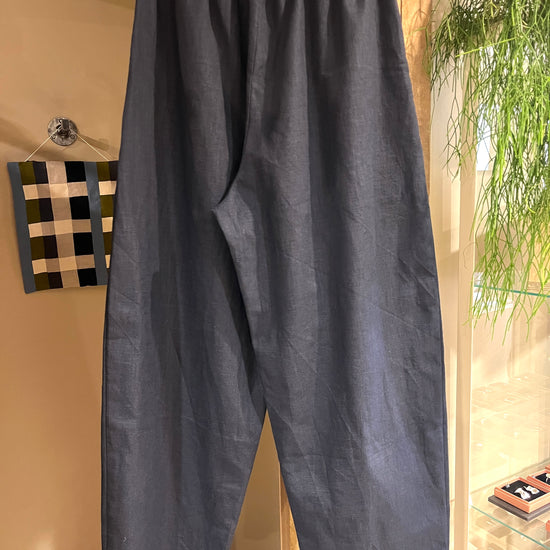 Navy blue barrel leg linen pants with an elastic waistband hanging on a metal hanger in an indoor boutique setting.