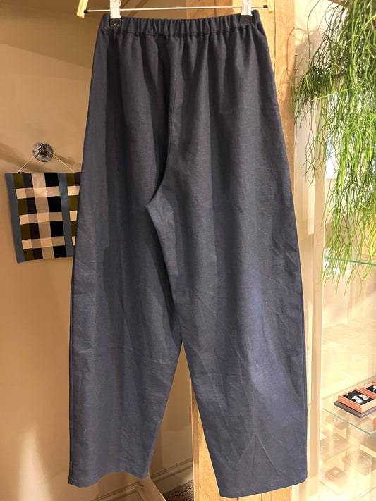 Navy blue barrel leg linen pants with an elastic waistband hanging on a metal hanger in an indoor boutique setting.