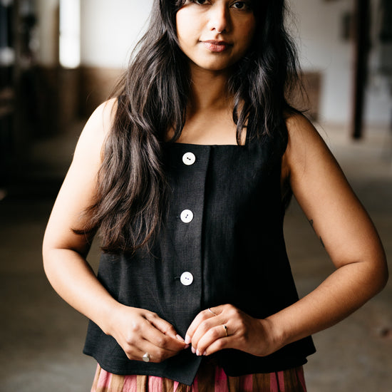 Woman wearing a black sleeveless top with buttons and a plaid skirt in an indoor setting.