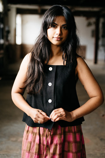Woman wearing a black sleeveless top with buttons and a plaid skirt in an indoor setting.