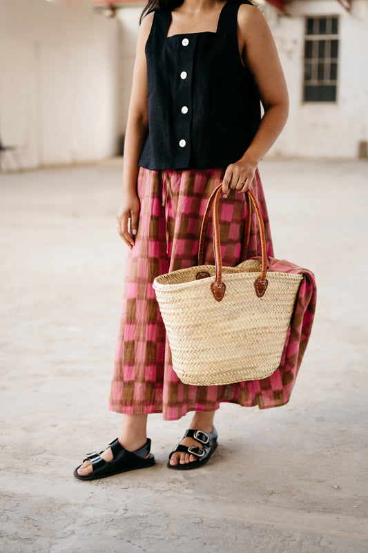 Person wearing a black top and pink plaid skirt holding a straw bag.