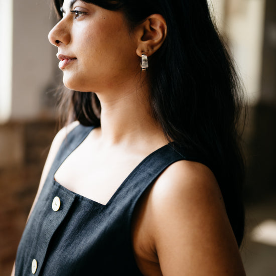 Woman wearing a black sleeveless top with white buttons, standing indoors.