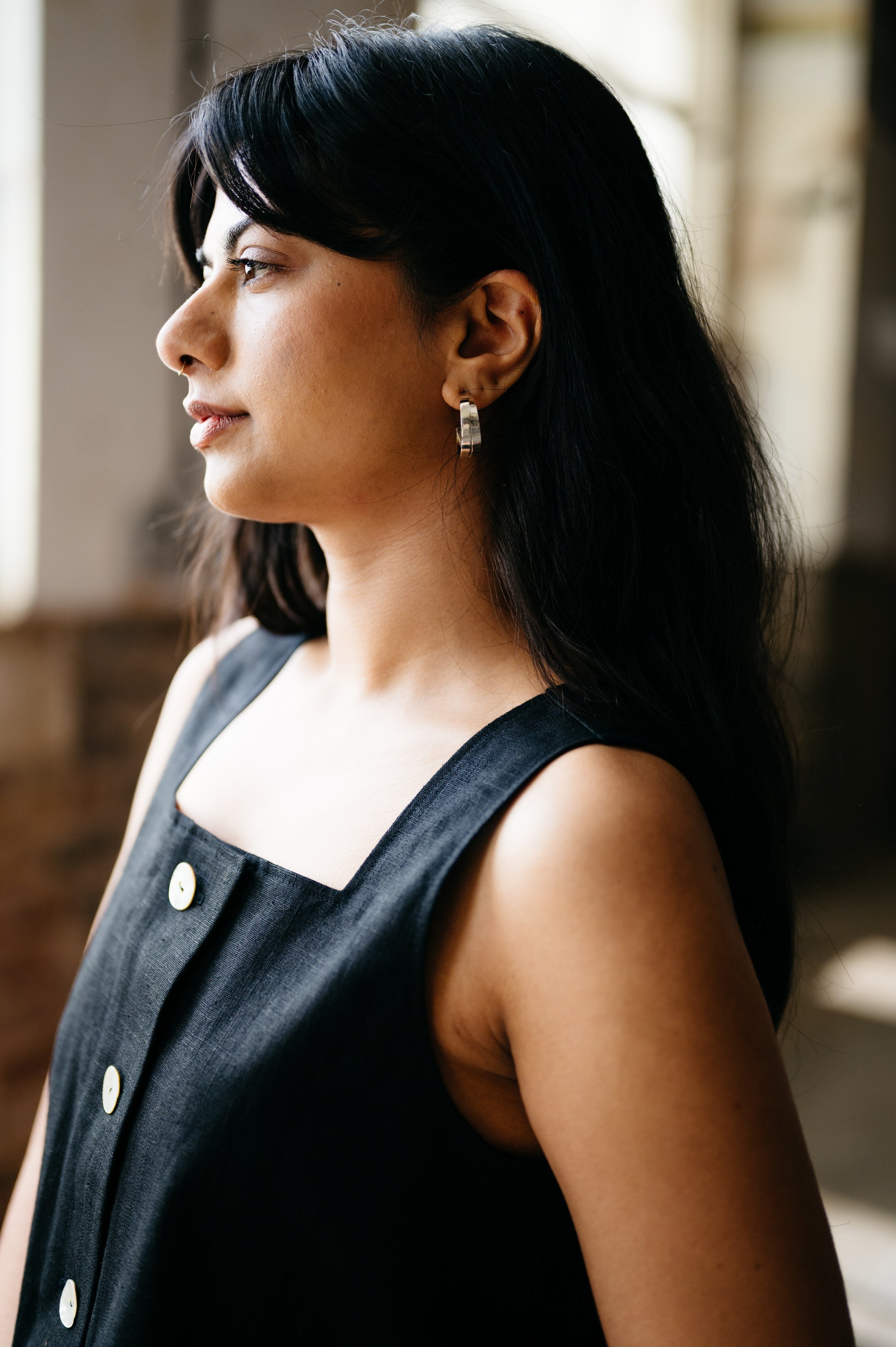 Woman wearing a black sleeveless top with white buttons, standing indoors.
