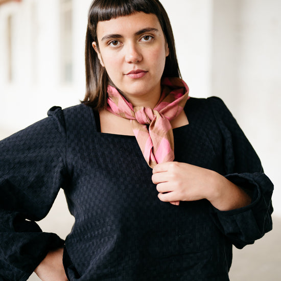 Model wearing a black textured long sleeve top and pink and brown ikat scarf in an indoor warehouse setting