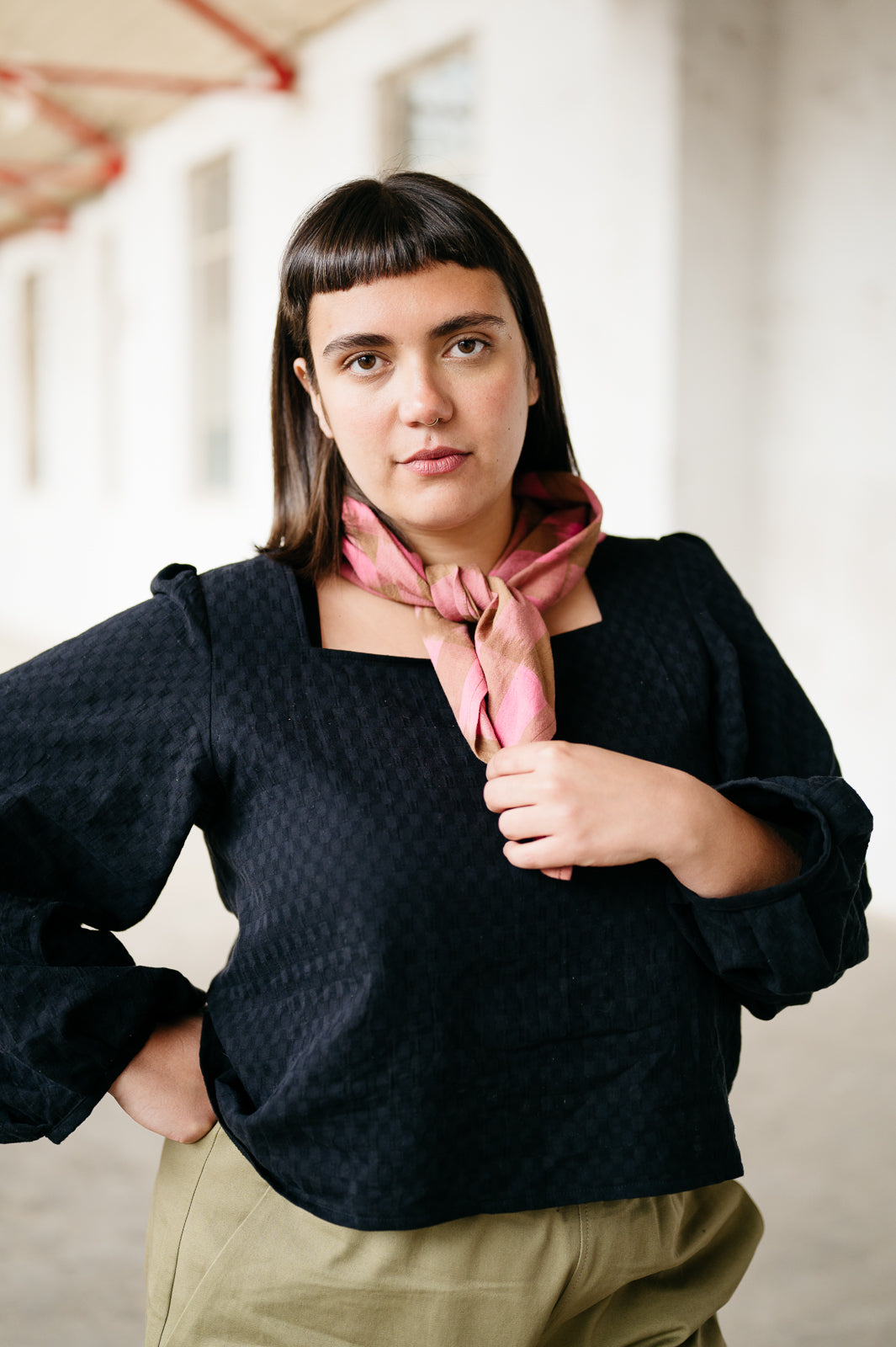 Model wearing a black textured long sleeve top and pink and brown ikat scarf in an indoor warehouse setting
