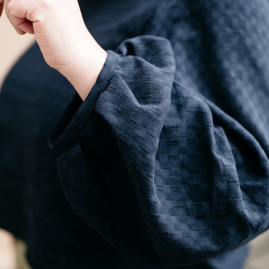 Close-up of a person wearing a black window pane fabric long sleeved top with a blurred background