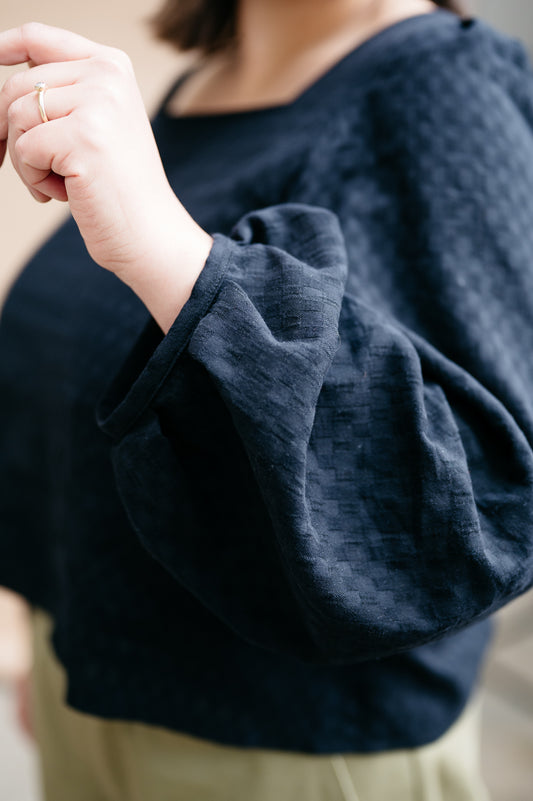 Close-up of a person wearing a black window pane fabric long sleeved top with a blurred background