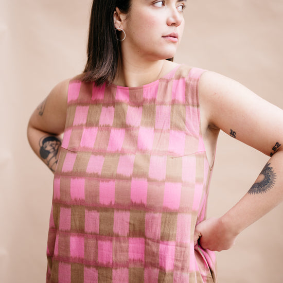 Woman wearing a pink and brown checkered dress against a beige background