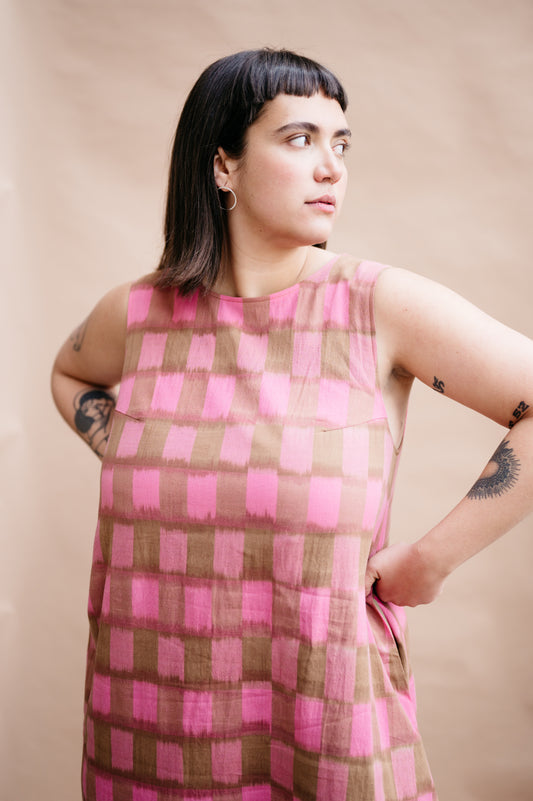 Woman wearing a pink and brown checkered dress against a beige background
