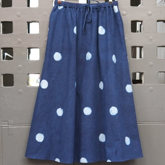 Polka dot indigo and pale blue block printed long skirt with drawstring waist tie on a wooden hanger in front of a grey grid door