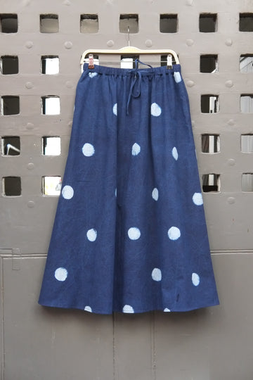 Polka dot indigo and pale blue block printed long skirt with drawstring waist tie on a wooden hanger in front of a grey grid door