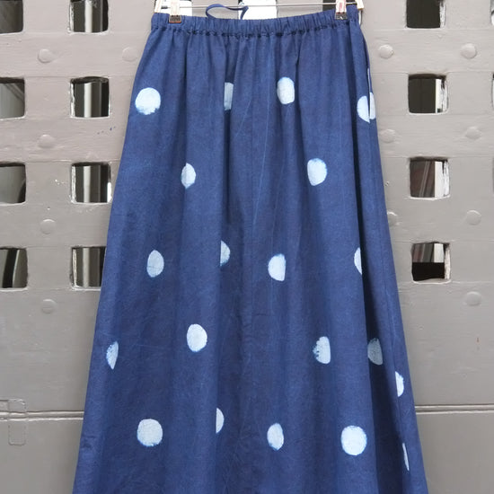 Polka dot indigo and pale blue block printed long skirt with drawstring waist tie on a wooden hanger in front of a grey grid door