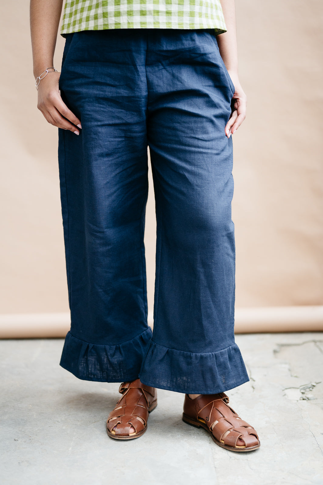 Person wearing navy blue trousers with ruffled cuffs against a beige background and brown sandals
