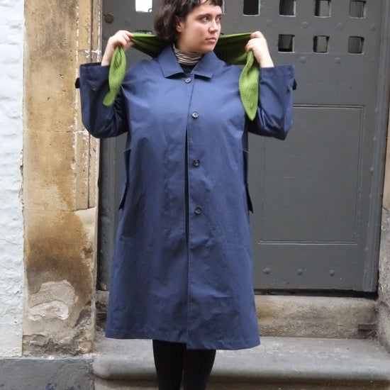 Person wearing a long blue coat standing in front of a metal gate.