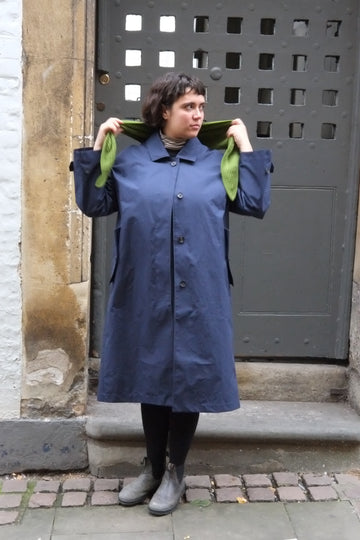 Person wearing a long blue coat standing in front of a metal gate.