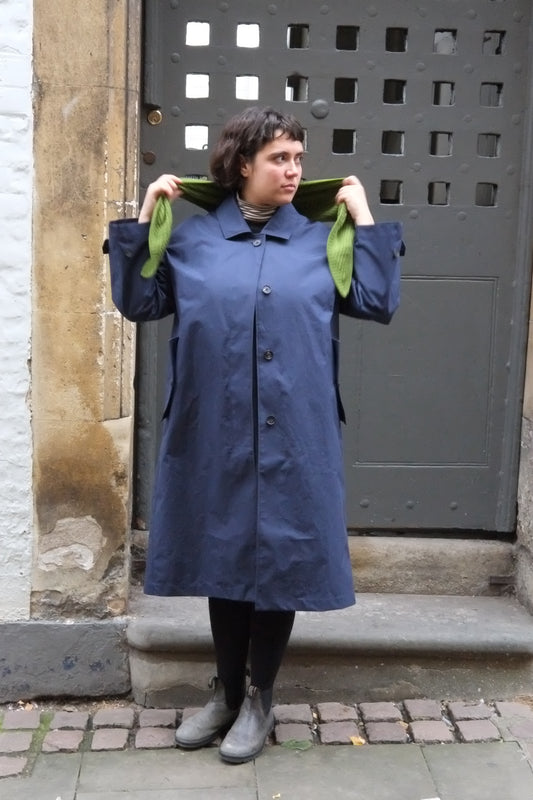 Person wearing a long blue coat standing in front of a metal gate.