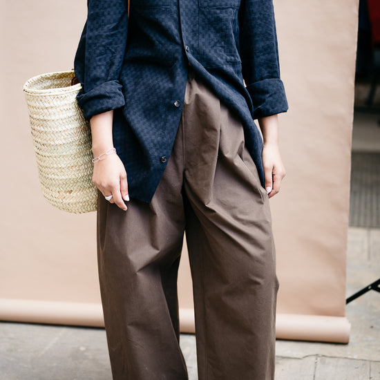 Person wearing a black shirt and brown trousers  holding a woven basket with red shoes on