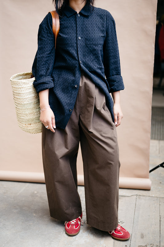 Person wearing a black shirt and brown trousers  holding a woven basket with red shoes on