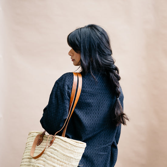 Person wearing a black textured loose fitting oversized shirt with a straw bag on a beige background