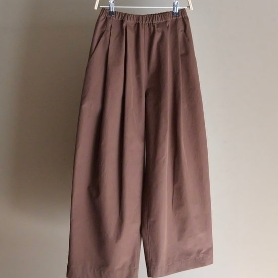 Brown pants hanging on a white hanger against a plain background