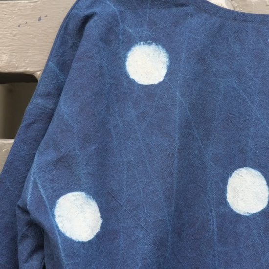 An indigo blue long-sleeve top with white polka dots hanging on a wooden hanger against a grey grid door