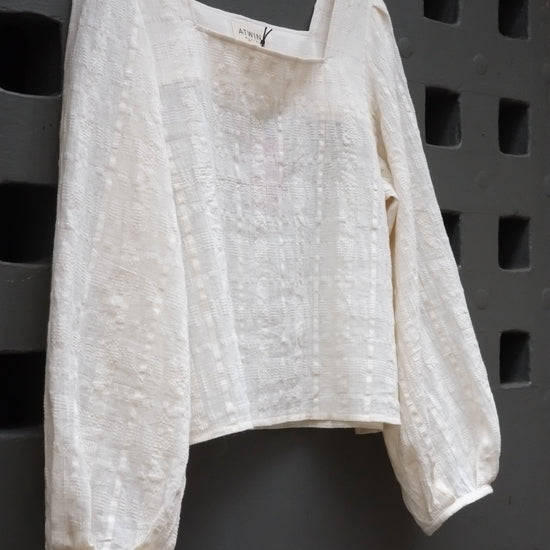 A white textured blouse on a grey background.