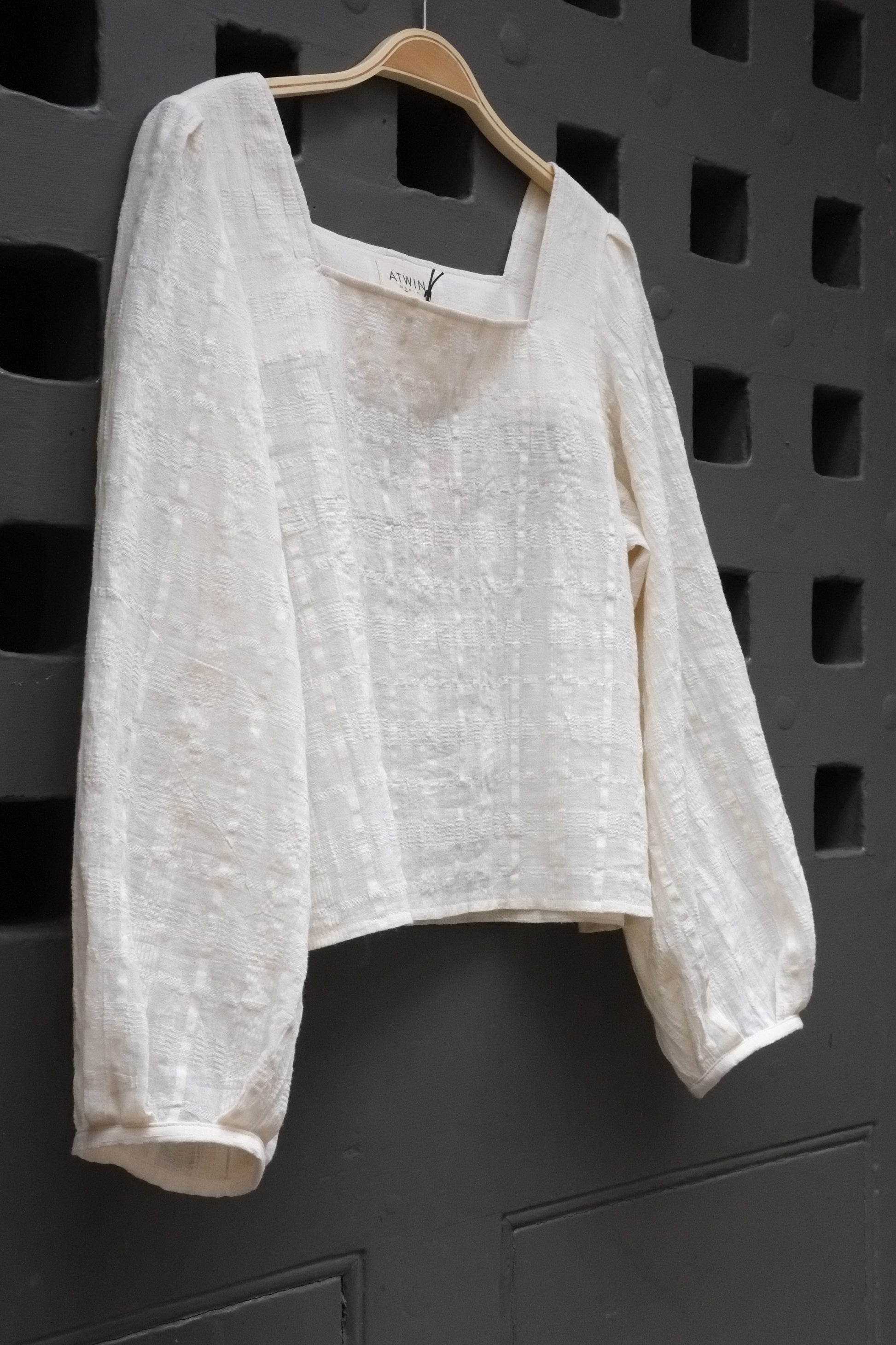 A white textured blouse on a grey background.