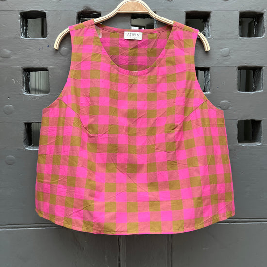 Fuchsia pink and khaki green checked cotton sleeveless tank top on a wooden hanger against a grey door