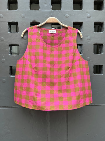 Fuchsia pink and khaki green checked cotton sleeveless tank top on a wooden hanger against a grey door