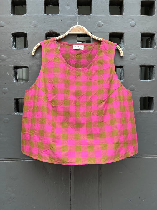 Fuchsia pink and khaki green checked cotton sleeveless tank top on a wooden hanger against a grey door
