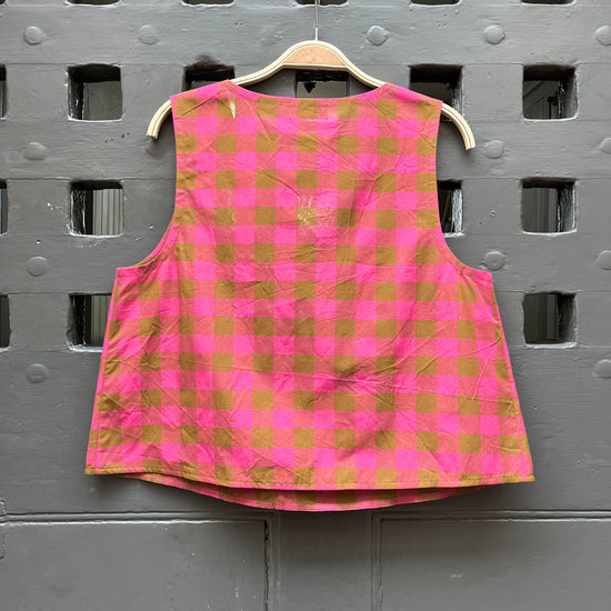 Fuchsia pink and khaki green checked cotton sleeveless tank top on a wooden hanger against a grey door