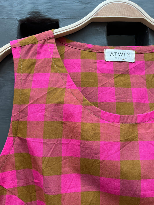 Fuchsia pink and khaki green checked cotton sleeveless tank top on a wooden hanger against a grey door