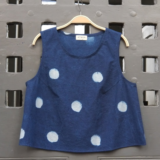 indigo denim and white  block moon print sleeveless tank top with round neck on a wooden hanger in front of a grey grid door