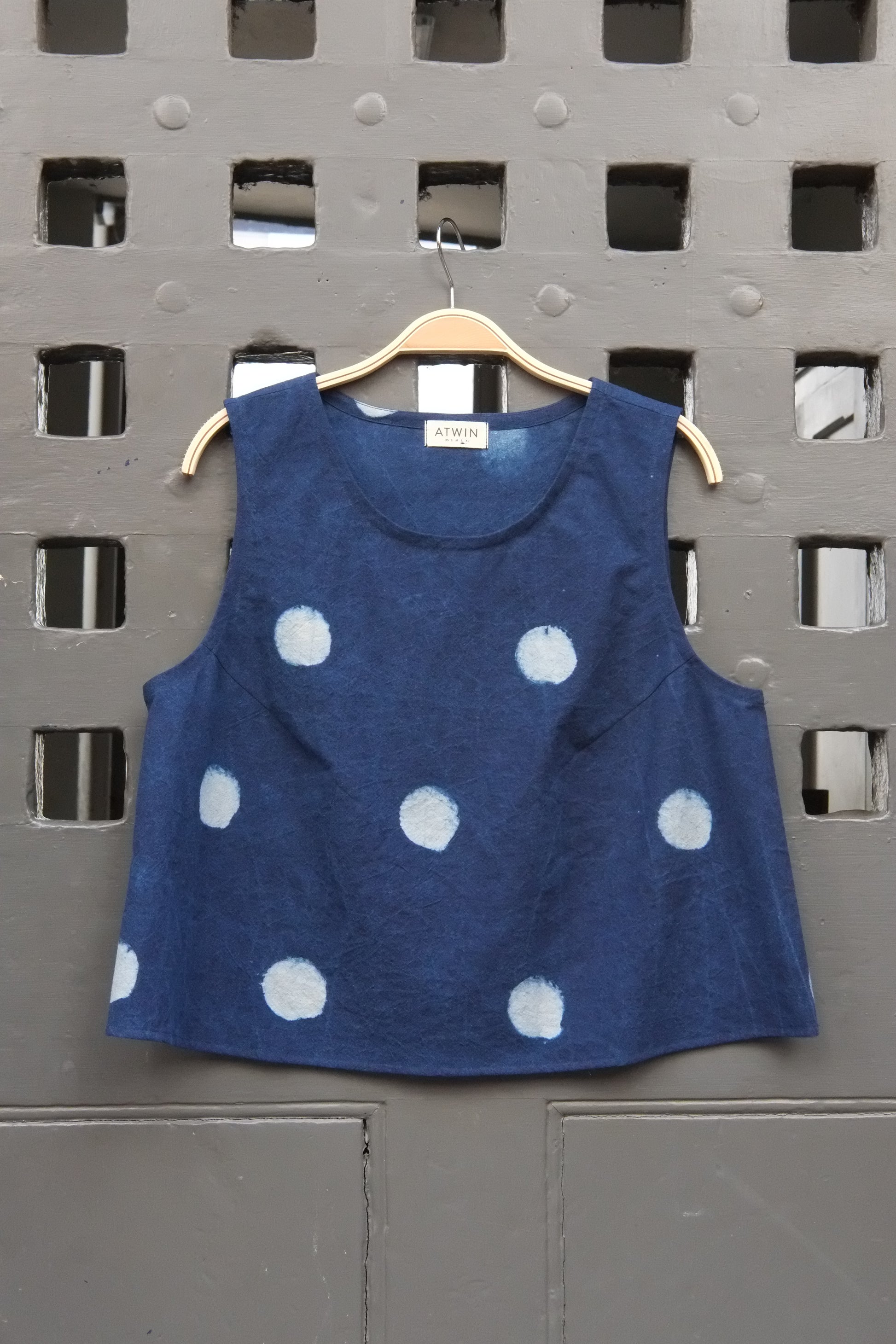 indigo denim and white  block moon print sleeveless tank top with round neck on a wooden hanger in front of a grey grid door