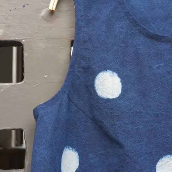 A sleeveless blue top with white polka dots hanging on a wooden hanger against a grey door.