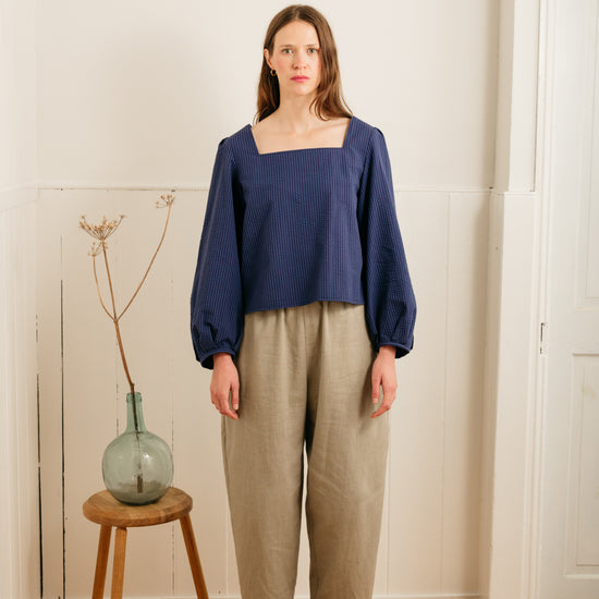 woman wearing atwin the label grain barrel leg trousers with a blue top against a wall