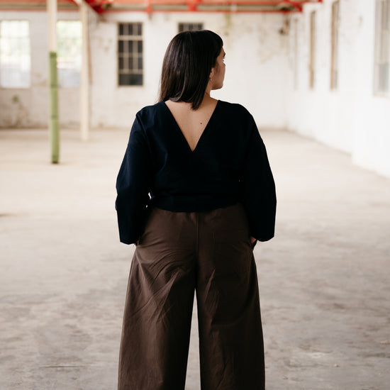 Person wearing a black top and brown wide-leg pants in an empty warehouse.