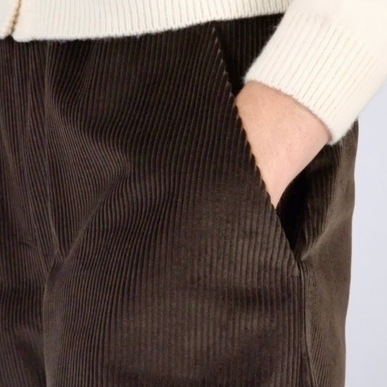 model wearing brown corduroy trousers with hands in pockets against a white backdrop