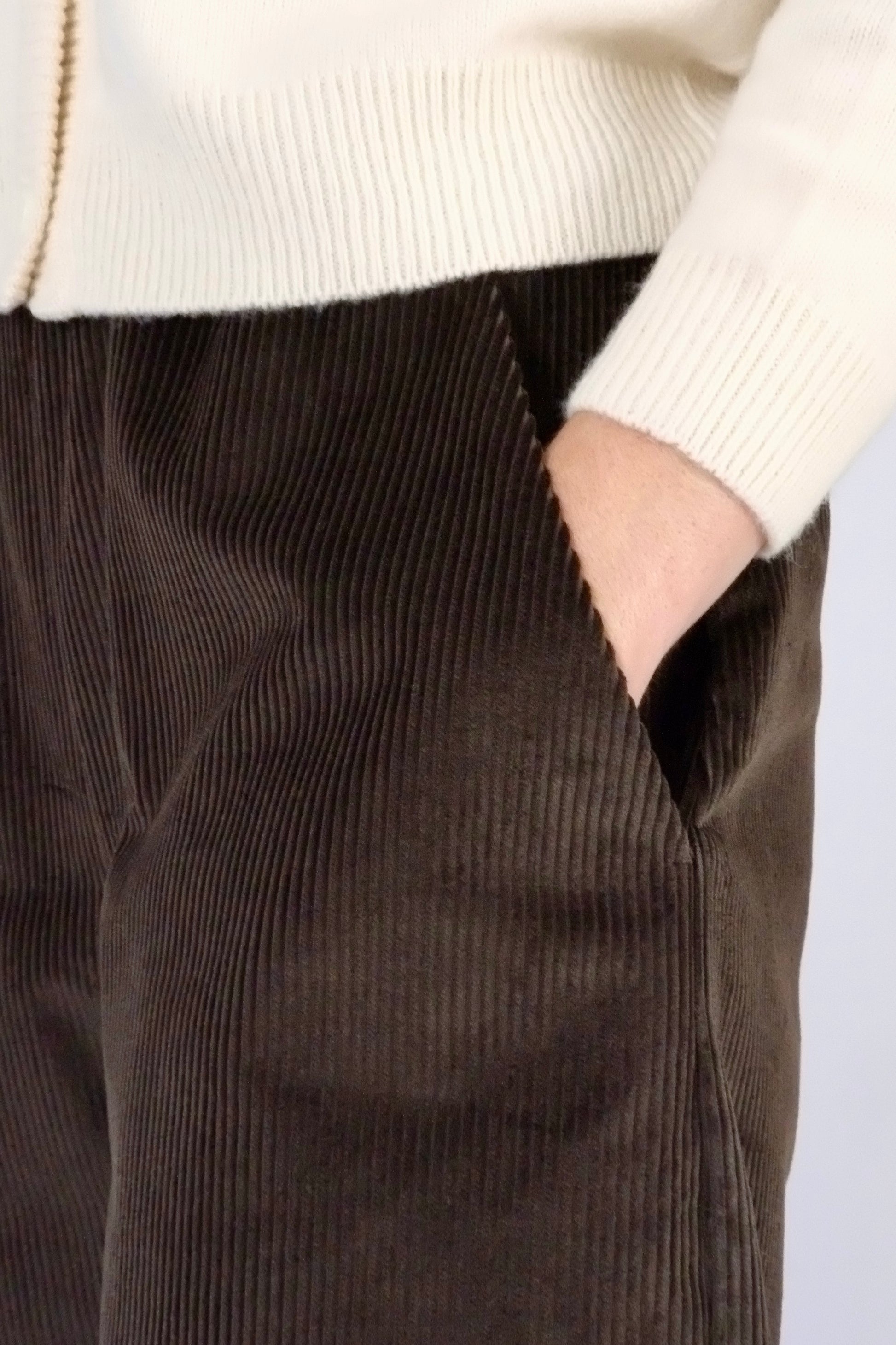 model wearing brown corduroy trousers with hands in pockets against a white backdrop