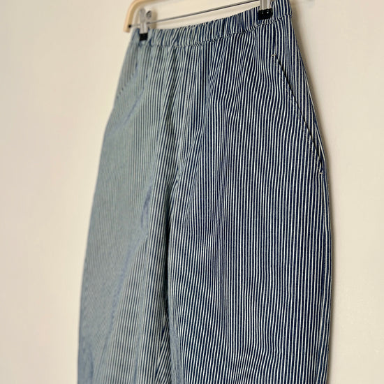 Blue and white striped denim trousers hanging on a wooden hanger against a beige wall.