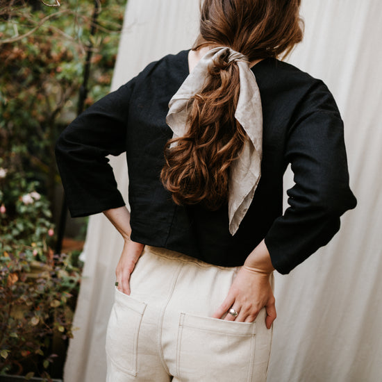 Person wearing a black top and beige pants with a scarf, standing outdoors.